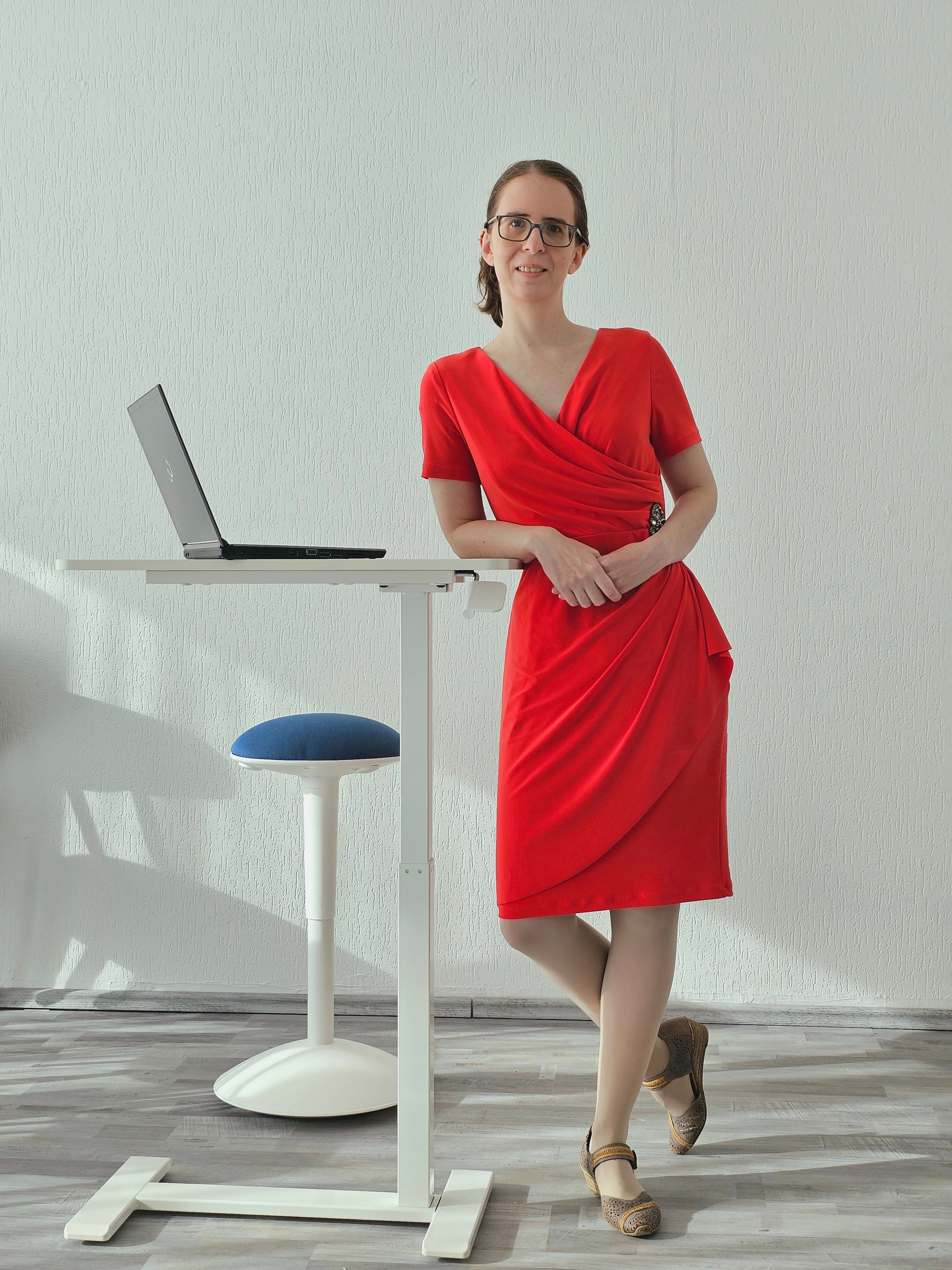 Inhaberin Katharina Basters in einem orangenen Kleid lehnt entspannt gegen ein Pult mit einem Laptop